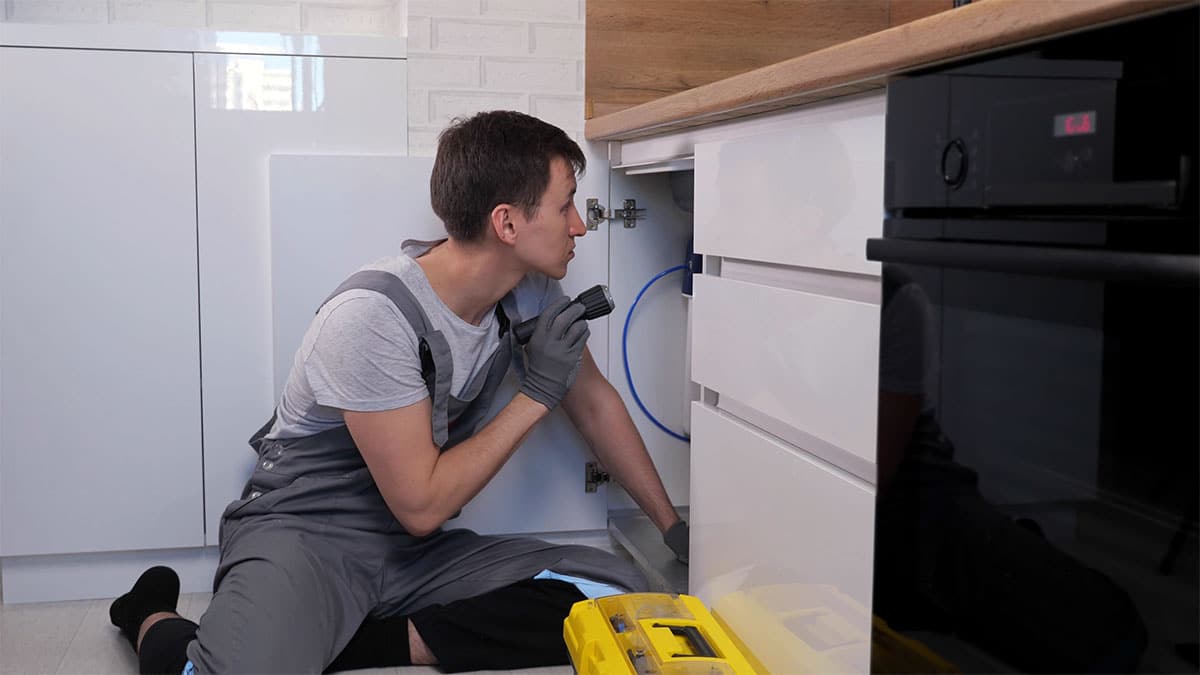 Ein Handwerker überprüft einen Wasseranschluss einer Küche.
